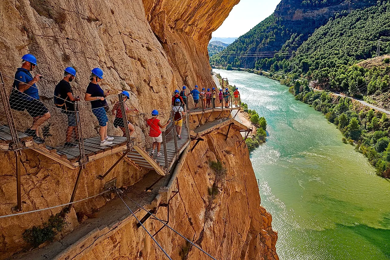 Walkers with helmets on the Caminito del Rey boardwalk above the green Guadalhorce river