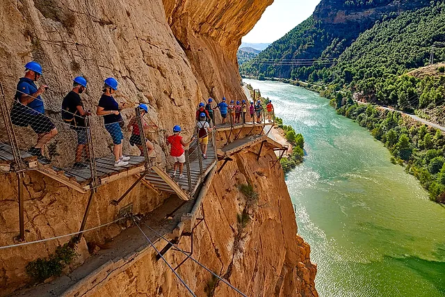 Walkers with helmets on the Caminito del Rey boardwalk above the green Guadalhorce river