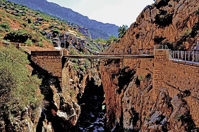 A bridge spanning the gorge between red cliffs on the Caminito del Rey